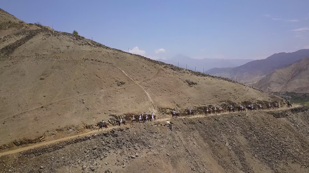Riders on horseback traverse a rugged desert landscape under a clear blue sky. A striking image for travel, adventure, and cultural storytelling.