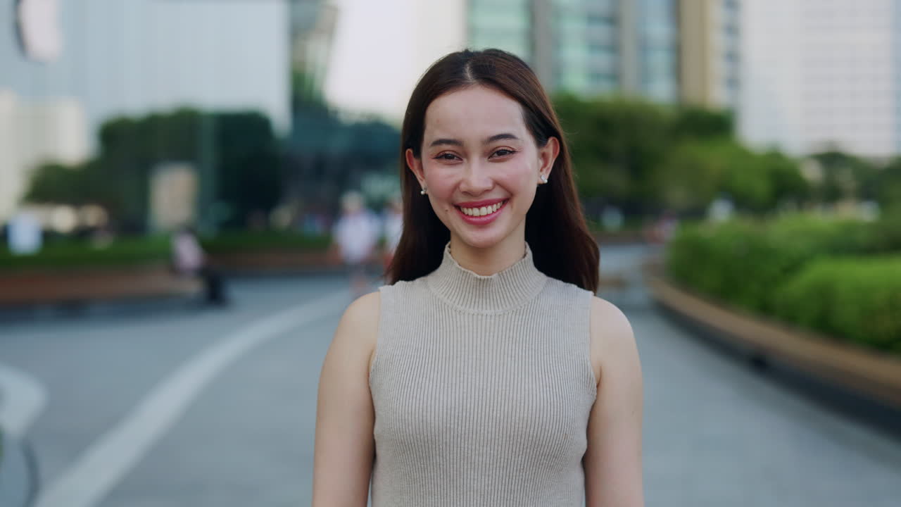 หญิงสาวชาวเอเชียกำลังยิ้มให้กล้องในสวนสาธารณะในเมือง