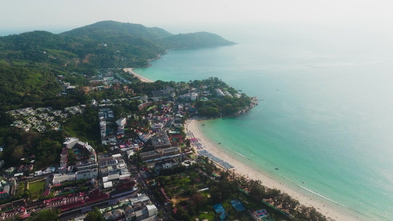 Dron avanza sobre una brumosa ciudad turística de Phuket hacia una bahía turquesa.