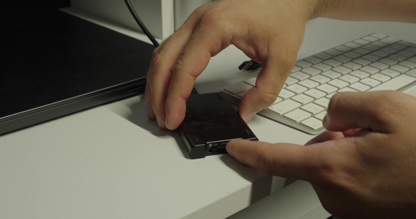 Close-up of a person inserting and removing a memory card from a USB card reader connected to a computer.