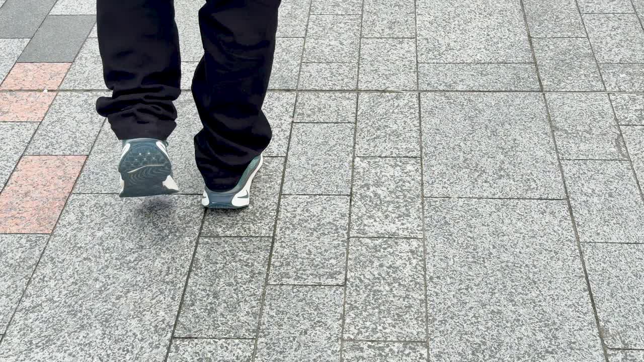 A person in dark trousers and sneakers walks away on a stone-paved Tokyo sidewalk