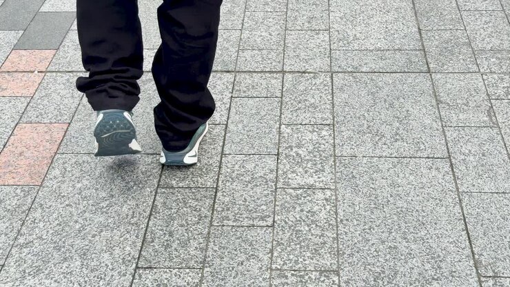 A person in dark trousers and sneakers walks away on a stone-paved Tokyo sidewalk