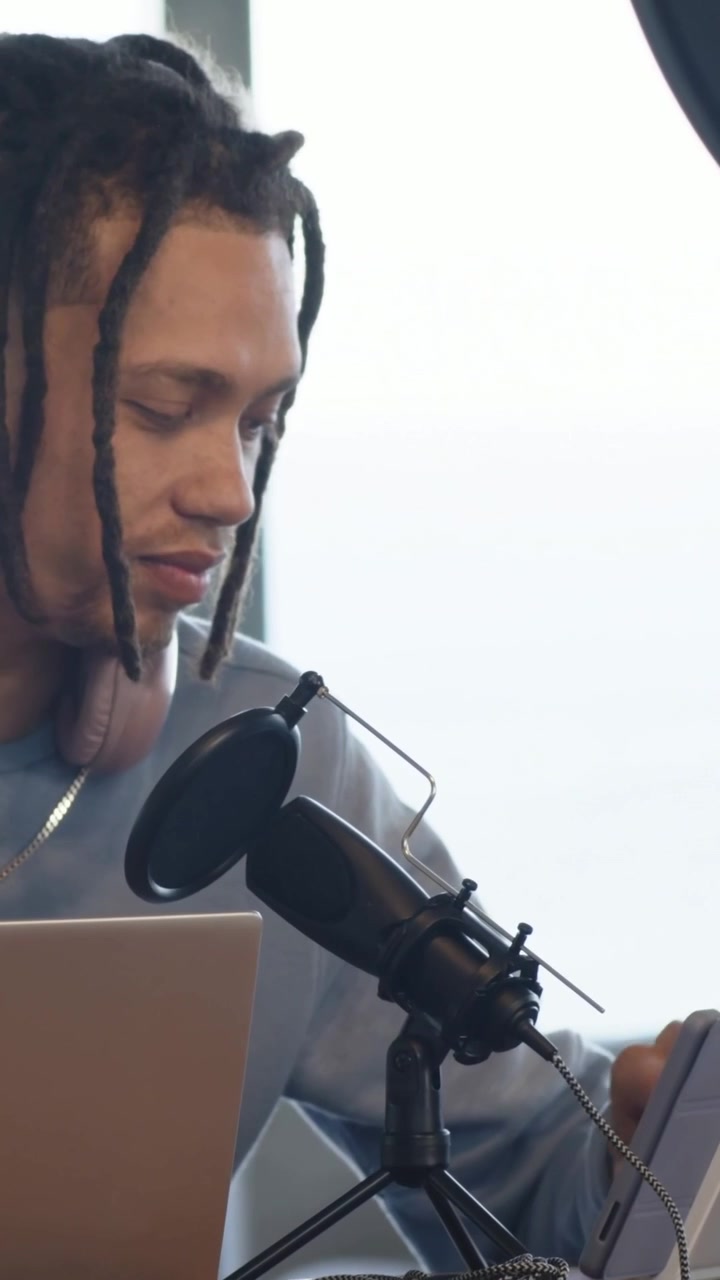 Video verticale: Uomo che guarda dal laptop al microfono, toccando il tablet mentre si prepara in studio, con spazio per il testo