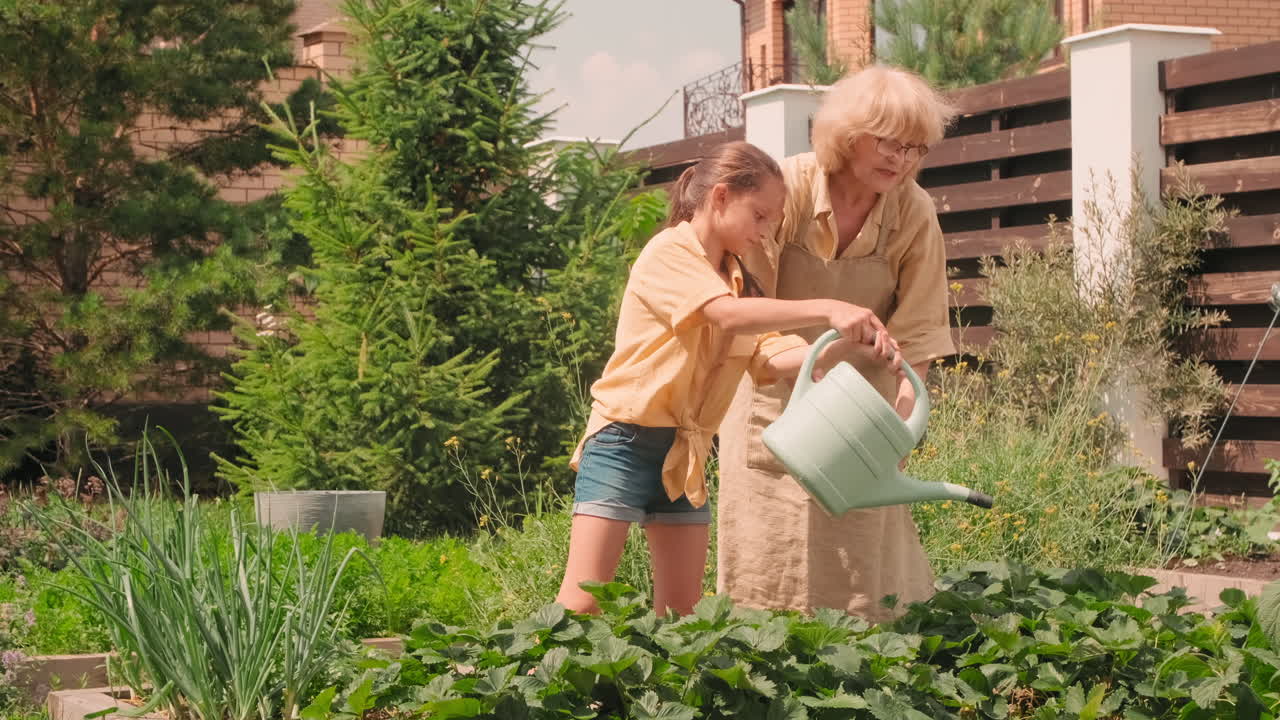 Girl With Grandmother Watering Flowers In Garden