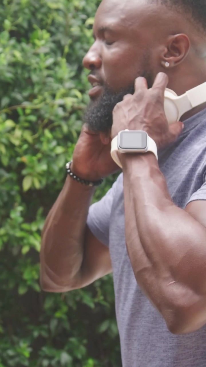 Vertical video: Straightening man in fitted tee placing over-ear headphones at patio checking fit