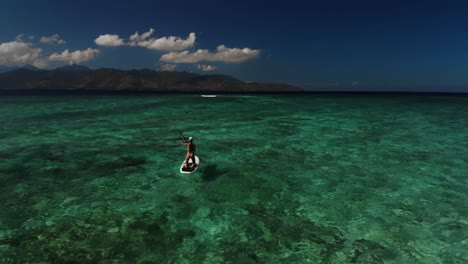 female person on sup paddleboarding on tropical ocean turquoise blue water