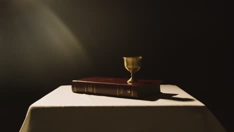 concepto religioso filmado con biblia y cáliz en el altar en un charco de luz