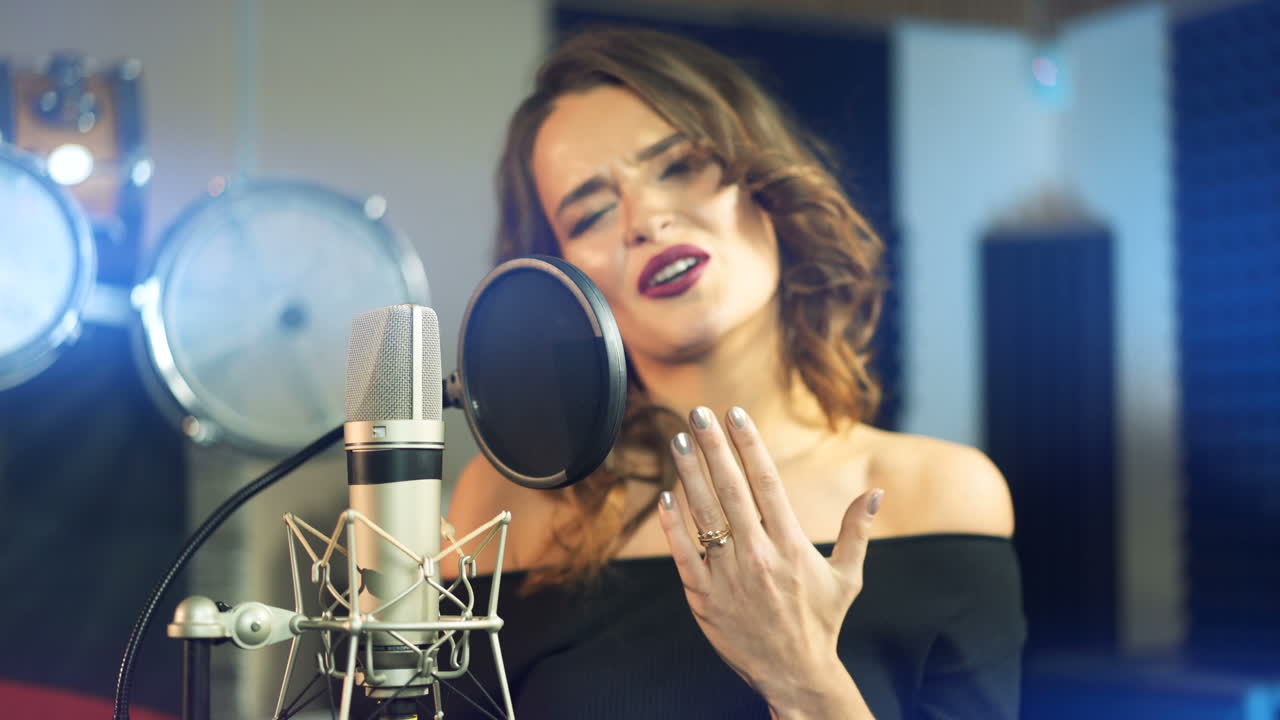 young singer is singing and recording a song in the audio studio on a blue background. Close-up