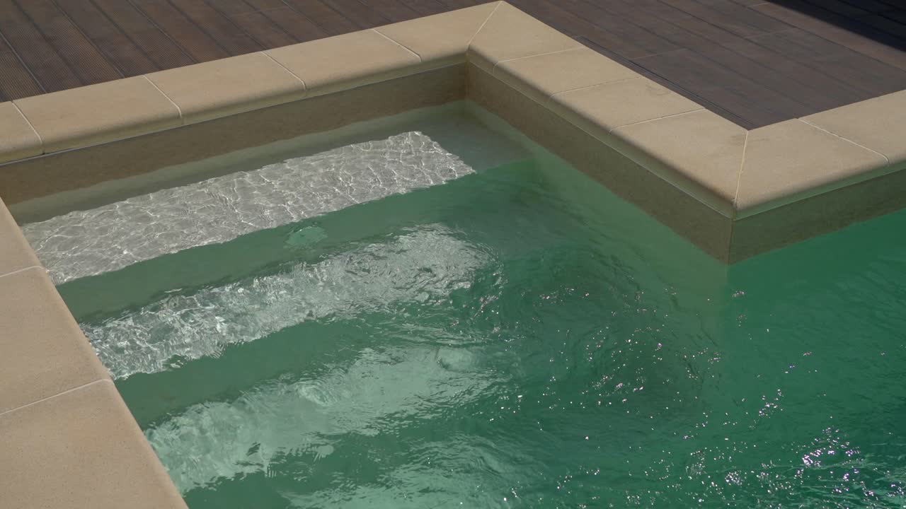 Clear water flowing in a corner swimming pool with built in steps and a wooden deck.