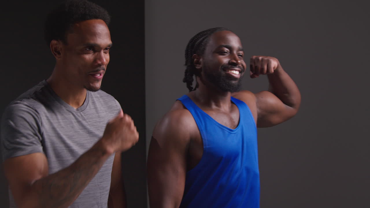 Studio Portrait Of Smiling Athletic Male Friends In Fitness Clothing Training Fist Bumping Shot Against Black Background