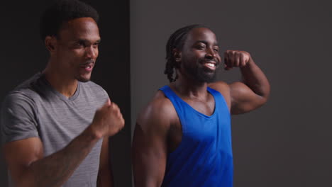 studio portrait of smiling athletic male friends in fitness clothing training fist bumping shot against black background