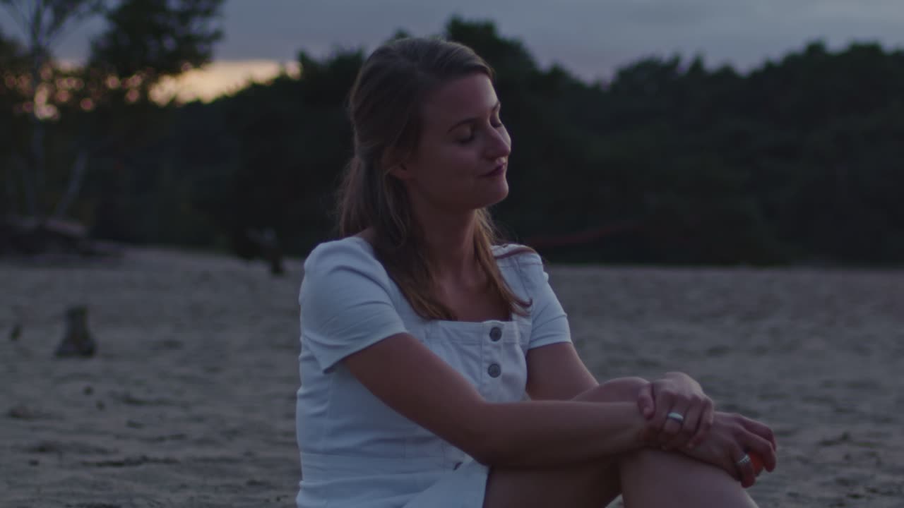 atractiva mujer joven sentada en las dunas de arena al atardecer