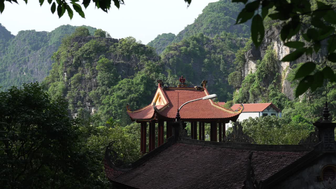 Buddhist Bích Động Pagoda with red-tiled roofs, nestled among lush green limestone karst mountains and tropical forest, Ninh Bình, Vietnam, Asia
