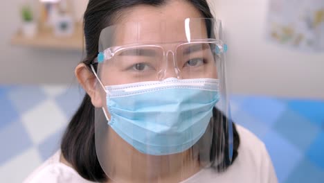 portrait of an asia young female who is wearing a face shield with mask rounded around her face from a frontal perspective to protect her glasses and eyes, scene of slow motion