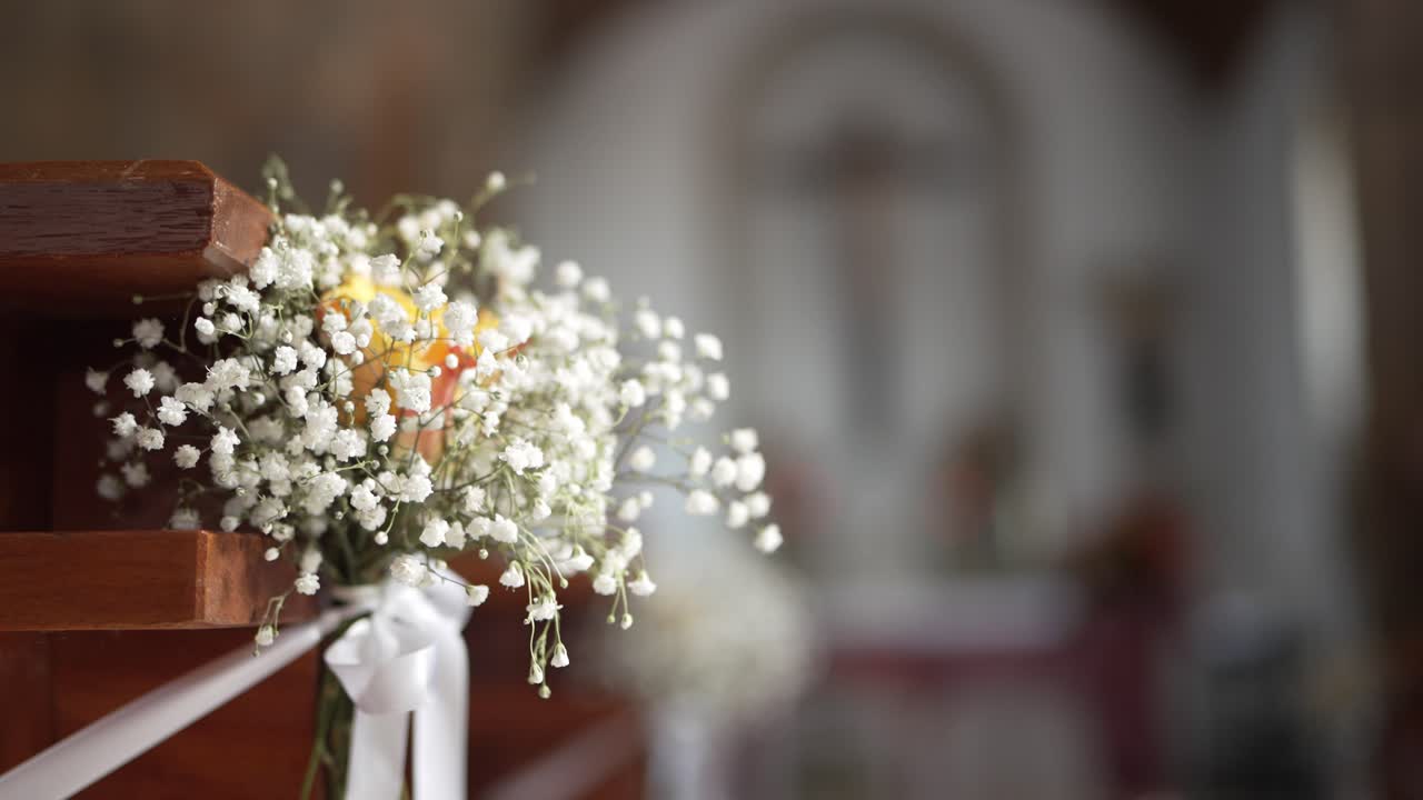 el aliento del bebé y el ramo de flores amarillas atado a un banco con una cinta blanca en una capilla