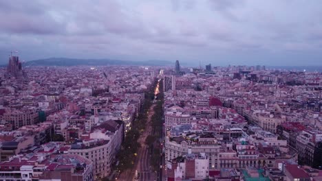 Luftaufnahme-Der-Skyline-Von-Barcelona-In-Der-Dämmerung-Mit-Beginnenden-Lichtern-Der-Stadt,-Düsterer-Himmel