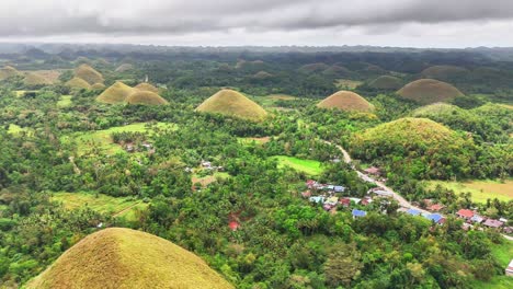 stunning aerial pull out shot reveals the iconic chocolate hills of bohol, philippines, scattered across lush tropical forest and villages under dramatic overcast skies on a humid day