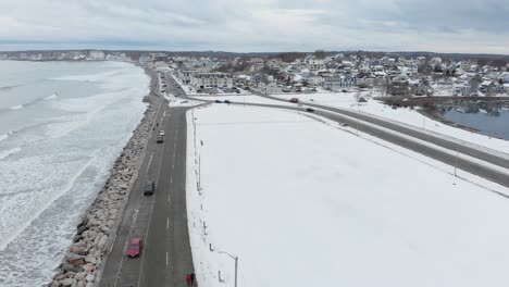 Hermosa-Escena-Nevada-Con-El-Océano-Y-La-Ciudad-En-El-Fondo,-Paneo-De-Drones-A-La-Izquierda