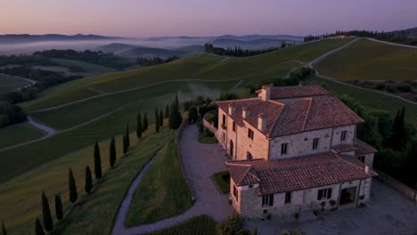 Stunning aerial view of a tuscan villa in the vineyards, bathed in the warm light of sunrise, with rolling hills, cypress trees, and a touch of mist adding to the serene atmosphere