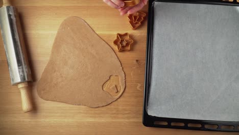 making shapes from gingerbread dough on a wooden table and placing them to baking tin topdown video