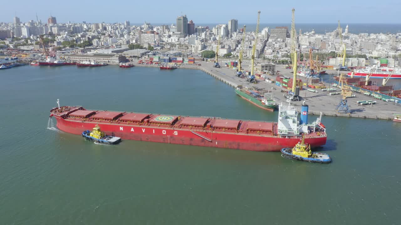 Bulk carrier Navios Sphera arriving to port with assistance of tug boats. Circling aerial side view