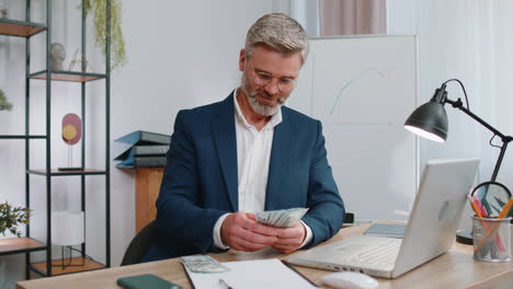 hombre de negocios rico en traje trabajando en una computadora portátil contando dinero en efectivo, calcular ganancias ingresos ganancias