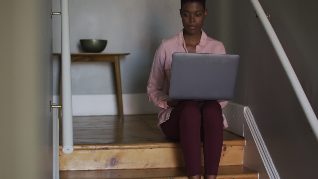 African american woman using laptop while sitting on stairs working from home