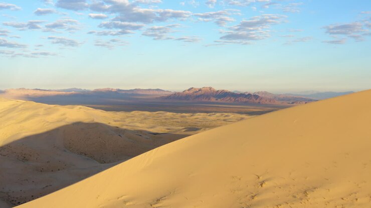 Een ronddraaiend beeld toont een uitzicht op verre woestijnbergen van achter een grote zandduin bij de Kelso Duinen in de Mojavewoestijn.