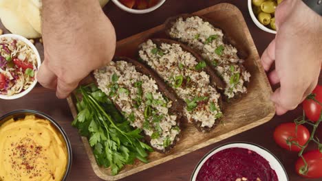 israeli cuisine. hands putting forshmak with black rye bread decorated with parsley close-up. national jewish herring dish, middle eastern culture. traditional snack vorschmack made of fish fillet