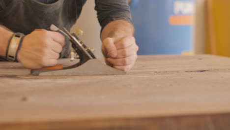 Un-Carpintero-Artesano-Experimentado-Está-Cepillando-A-Mano-Una-Mesa-De-Madera-Natural-Para-Quitar-Los-Bordes-ásperos-Y-Las-Protuberancias