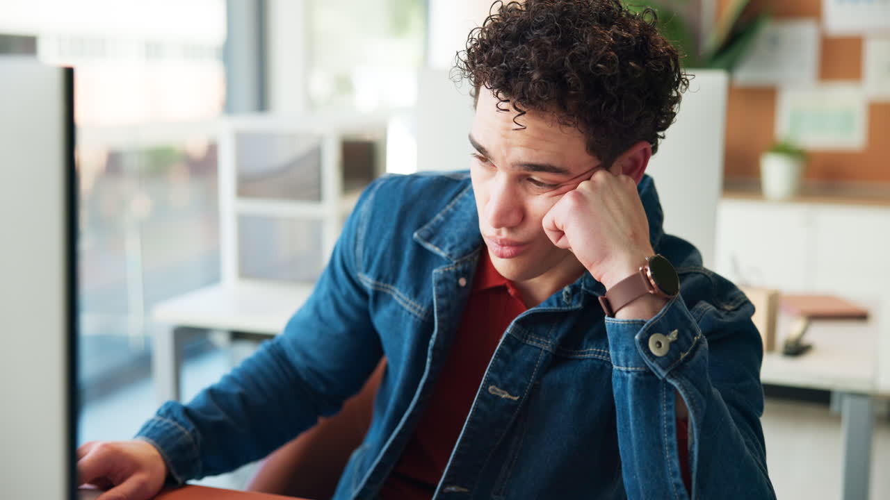 Jovem cansado apoiando a cabeça na mão enquanto trabalha no computador