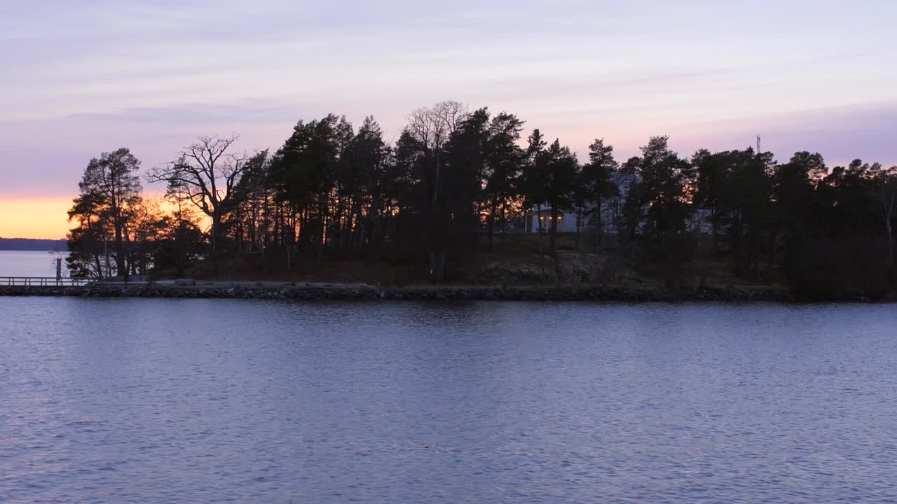 Slowmotion-optagelse af det smukke landskab med træer og solnedgangen over det strømmende vand ved en af Stockholms skærgårdsøer.