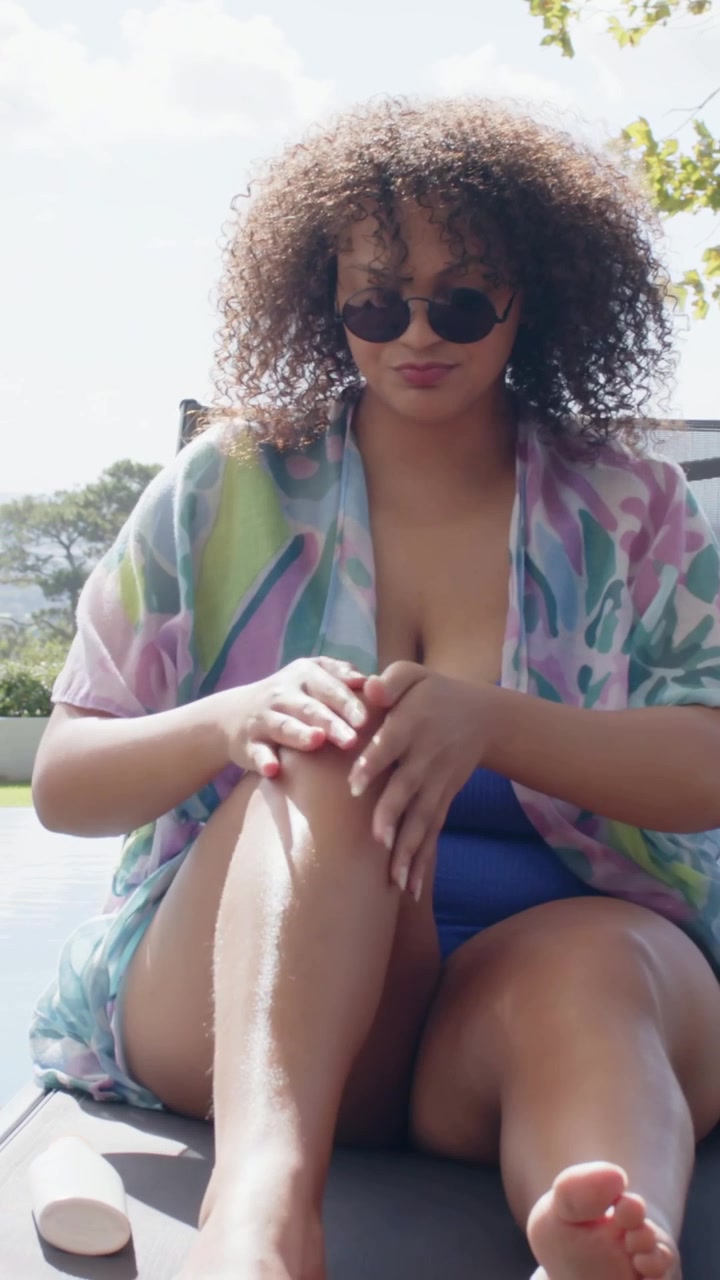 Vertical video: Rubbing leg woman in blue swimsuit reacting to sun, applying lotion by pool