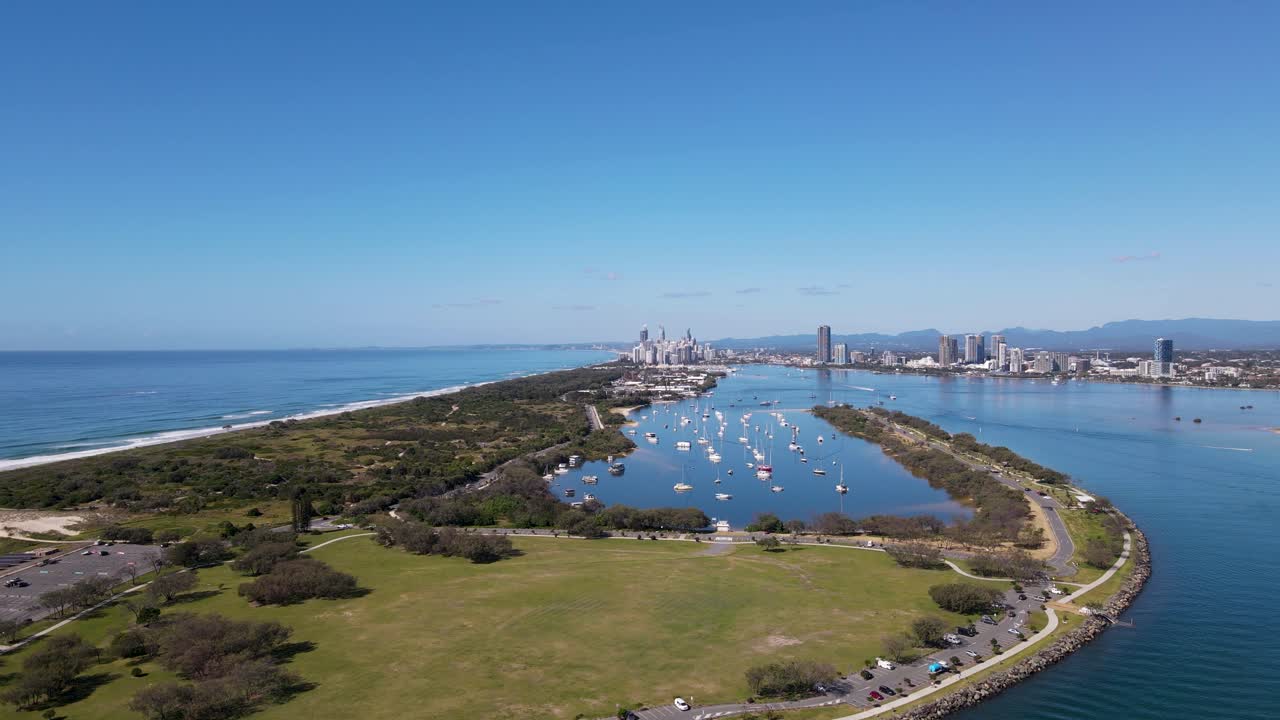 대도시의 스카이라인과 먼 산맥이 있는 인기 있는 도시 보트 항구를 향해 인공 섬을 여행하는 빠르게 움직이는 드론 전망