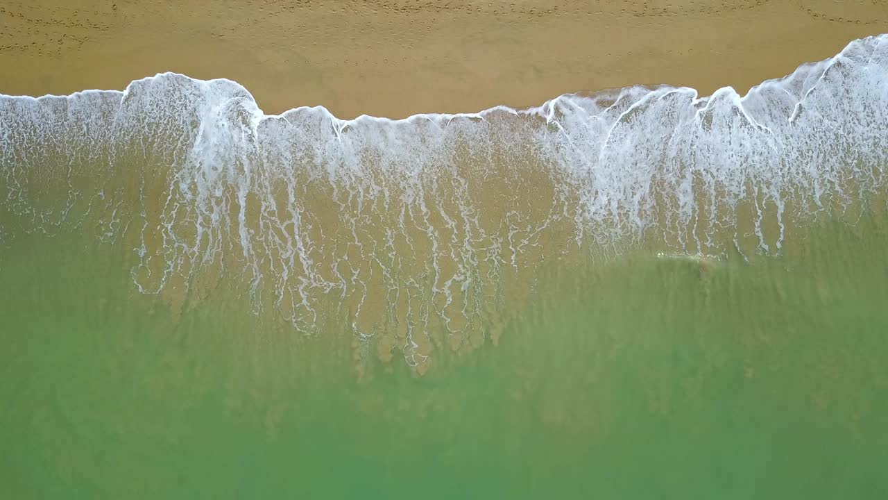 Aerial view of looping turquoise ocean wave reaching the coastline ...