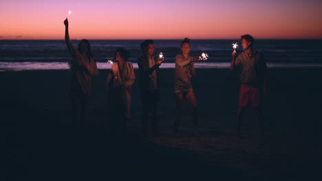 friends on the beach holding sparkers celebrating at sunset