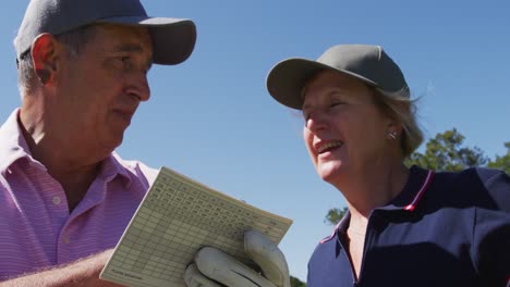 Pareja-Mayor-Caucásica-Escribiendo-Puntaje-De-Golf-En-El-Cuadro-De-Mando-En-El-Campo-De-Golf-En-Un-Día-Soleado