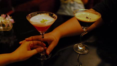 two hands clinking cocktails in a cozy setting