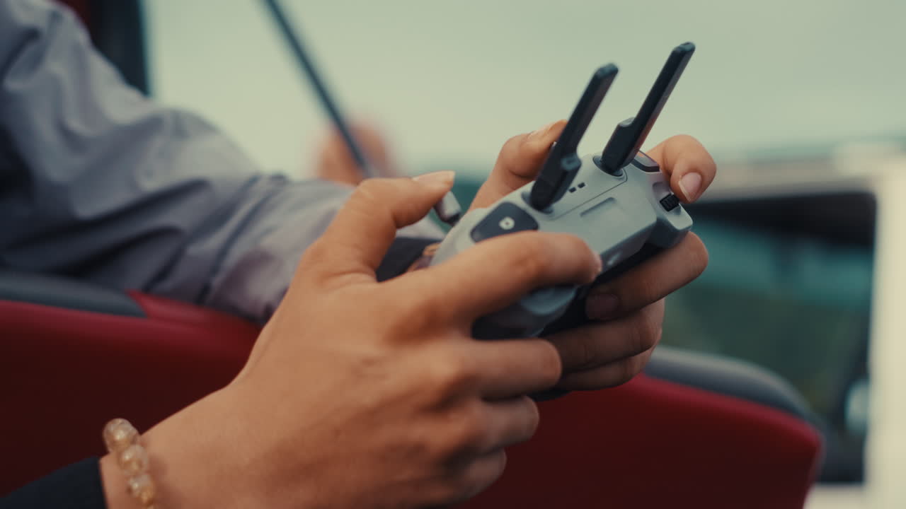 A cinematic close-up shot of a pilot's hands expertly navigating a drone remote controller with extended antennas, focusing on the precision of aerial cinematography