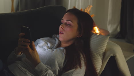 Woman-Lying-On-Sofa-At-Home-At-Night-Streaming-Or-Looking-At-Online-Content-On-Mobile-Phone-1