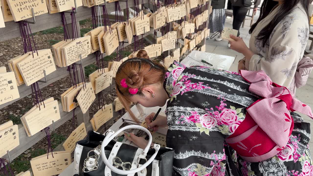 Wanita-wanita berkimono tradisional menulis doa di plakat ema kayu di Kuil Meiji Jingu.