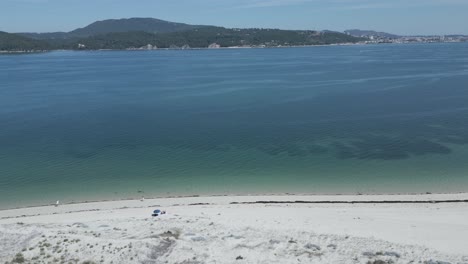Aerial-panoramic-view-of-the-Arrábida-coast,-hill-and-beaches-in-Setúbal-from-troia-island-with-people-walking-over-beach,-Portugal