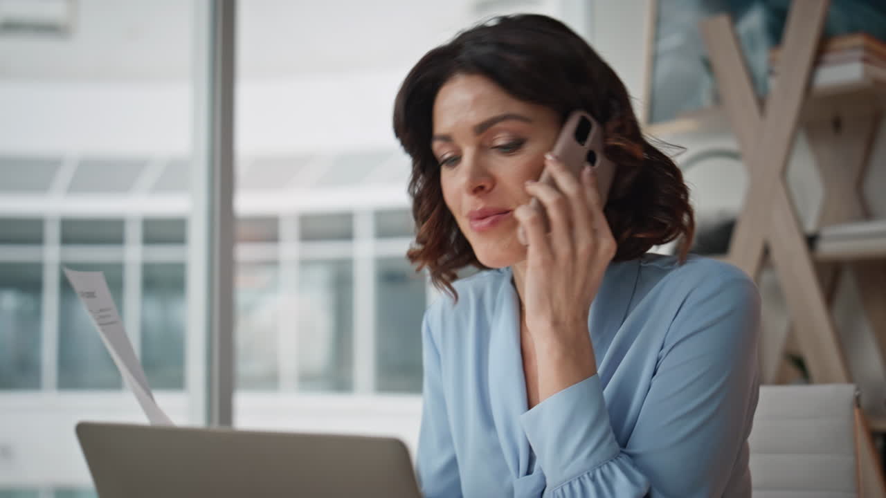 Happy employee talking mobile phone at office desk with laptop closeup smiling