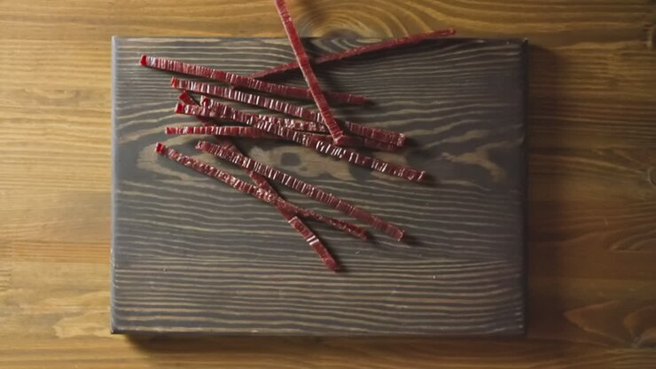 Männerhände lassen getrocknete rote Fisch-Sticks auf ein Holzbrett fallen.