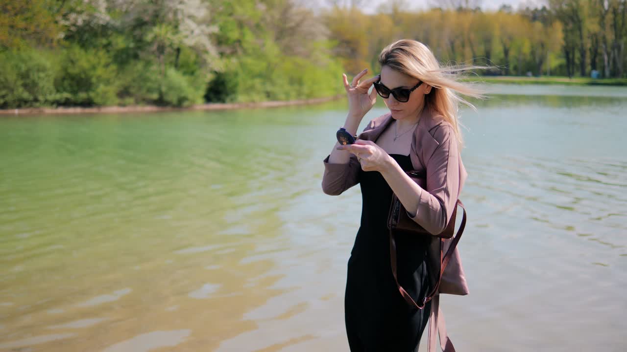 красивая молодая женщина исправляет свою прическу, глядя в зеркало на фоне красивой природы