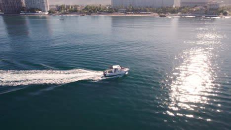 yacht at high speed, approaching and doing a frontal orbit, showing the coast of puerto vallarta and the reflections of the sun in the sea as the yacht cuts through the waves.