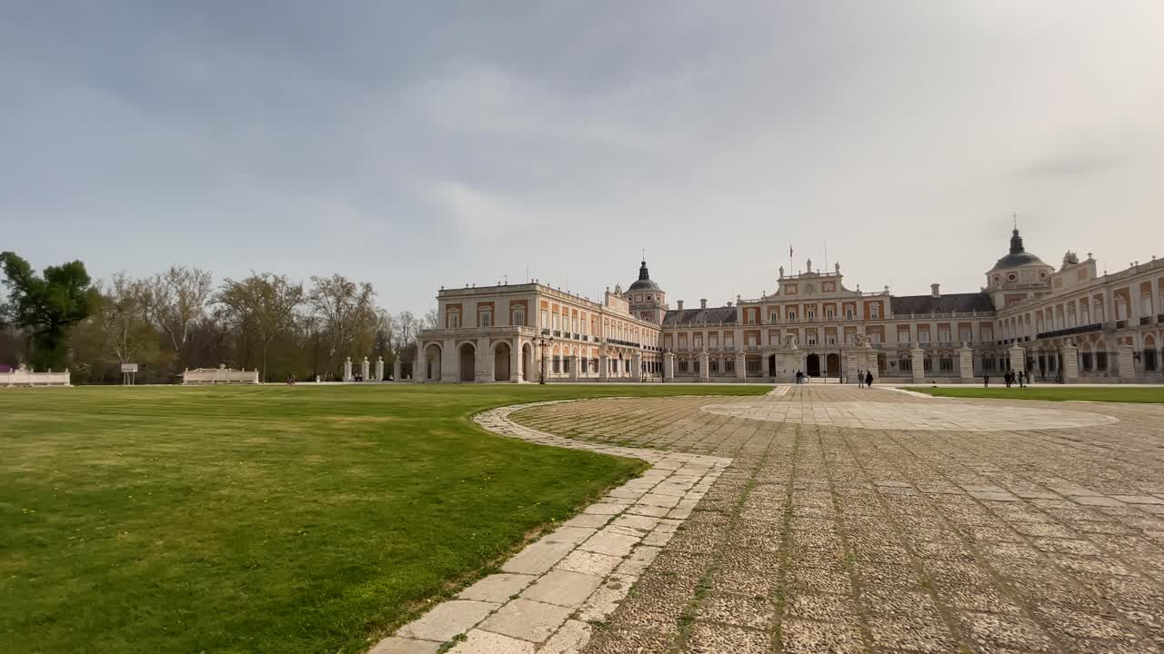 Beautiful filming of the imposing entrance front of the Royal Palace of Aranjuez from the Plaza de Armas, we appreciate its flooring and green grass, tourists appear strolling
