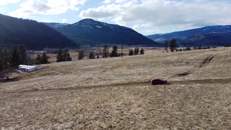 Orange-SUV-passing-through-fields,-beautiful-mountains,-and-clear-sky-in-the-background