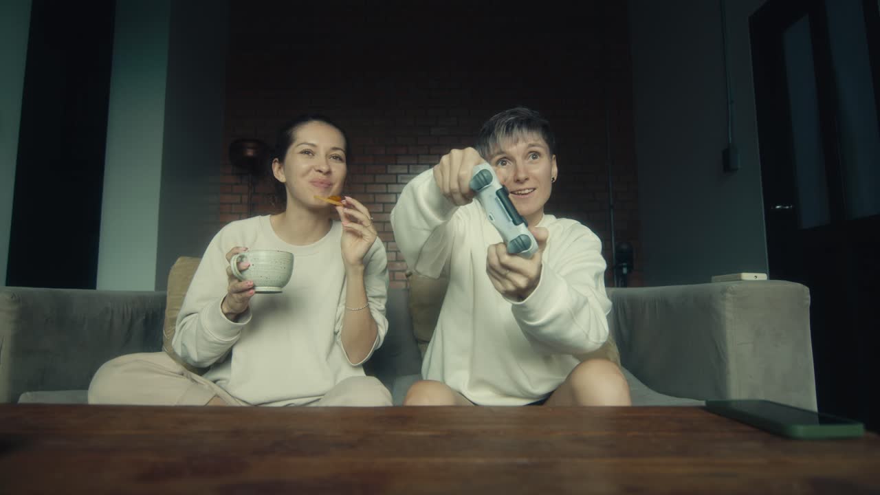 Two women friends playing video games on a couch