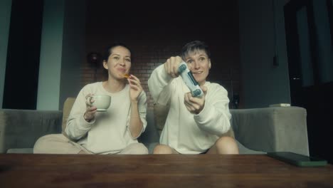 two women friends playing video games on a couch